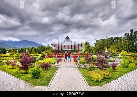 Coppia giovane in rosso controllato camicie azienda dalle mani e andando alla Pagoda giapponese giardino alla pioggia cielo nuvoloso Foto Stock