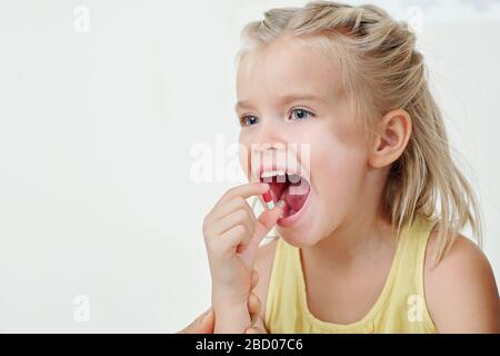 Positivo bella bionda bambina prendendo pillola di supplemento, vitamina o medicina Foto Stock