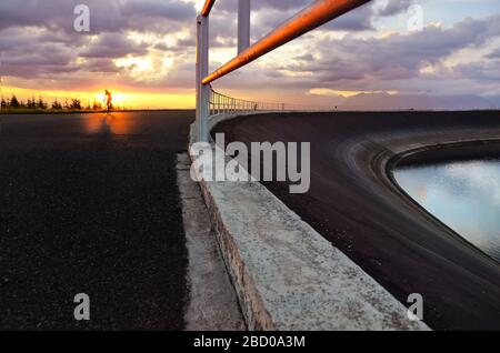 Giovane uomo in bicicletta attraverso il campo agricolo estivo durante il tramonto Foto Stock