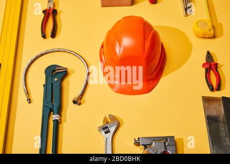 piatto con casco, pinze, chiave per scimmie, coltello per stucco, tubo idraulico, livella a bolla d'aria, nastro di misurazione e chiavi angolari su sfondo giallo Foto Stock