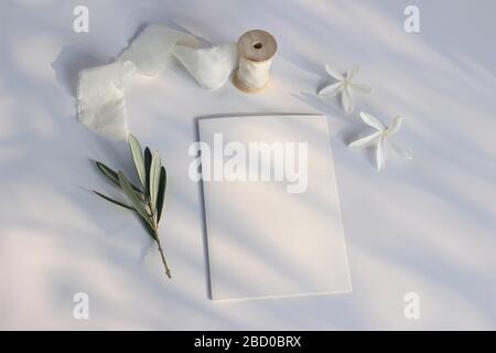 Estate matrimonio cancelleria mock-up scena. Biglietto d'auguri in bianco, invito, ramo d'oliva, macrocarpa bianca carissa, fiori di prugne natali e nastro di seta Foto Stock