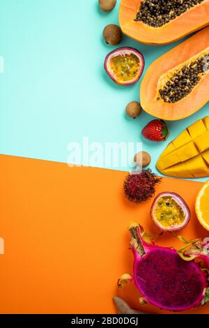 Colpo verticale di frutti tropicali su sfondo blu arancione. Layout creativo a base di papaia fresca, rambutan, mango, frutto della passione, arancio, longan, stra Foto Stock