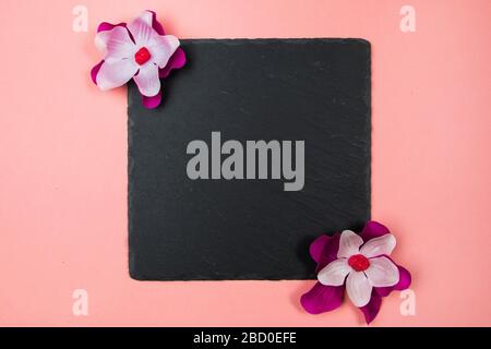 Quadrato nero con fiori viola e bianchi su sfondo rosa pastello Foto Stock