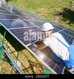 Montatore professionale che installa batterie solari su una carcassa metallica verde. Struttura di montaggio con trapano. Soluzione moderna per il risparmio di risorse naturali, utilizzando energia solare rinnovabile. Alta tecnologia. Foto Stock