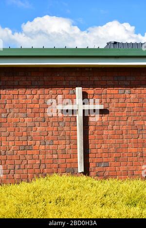 Croce cristiana in legno su pareti esterne in mattoni rossi di edificio chiesa contemporaneo. Foto Stock