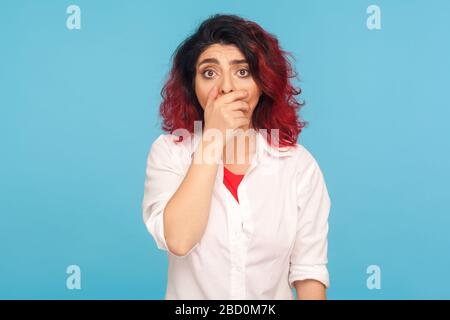 Ritratto di donna hipster spaventata con capelli rossi fantasia che coprono la bocca con la mano e guardando spaventato alla macchina fotografica, vittima intimidata paura di dire la verità Foto Stock
