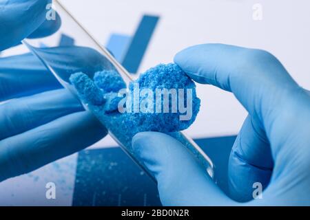 Lo scienziato mostra materiale in cristallo blu in mano e provetta in vetro in laboratorio Foto Stock