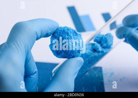 Il ricercatore mostra grande pezzo blu di cristallo in mano e provetta in vetro in laboratorio Foto Stock