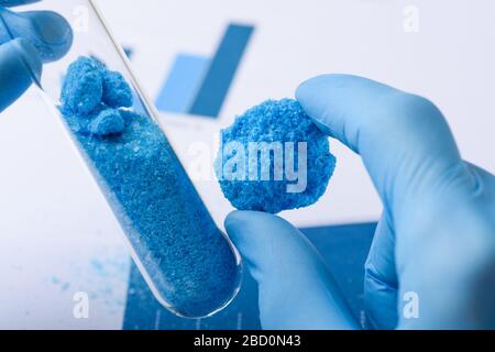 Materiale in cristallo blu in mano e provetta in vetro nel concetto di ricerca di laboratorio Foto Stock