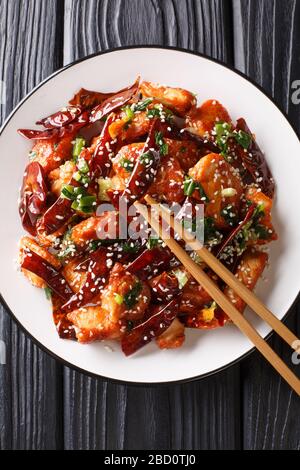 Croccanti e gustosi pezzi di pollo fritti con una generosa quantità di peperoncino secco e pepe Sichuan primo piano in un piatto sul tavolo. Vista verticale superiore Foto Stock