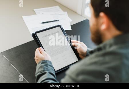 Uomo che legge il contratto di matrimonio su tablet in ufficio. Foto Stock