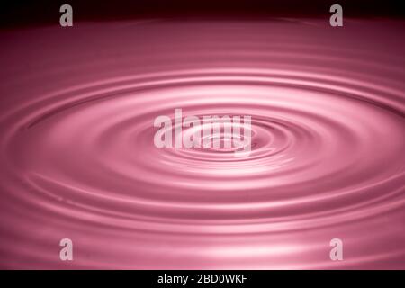 Gocce d'acqua spruzzano in un vetro di colore rosso Foto Stock