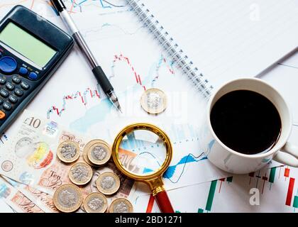 Alcuni soldi (libbre, sterling) calcolatrice, cappello di caffè, loupe e diversi grafici di soldi sulla tabella. Vista dall'alto. Foto Stock