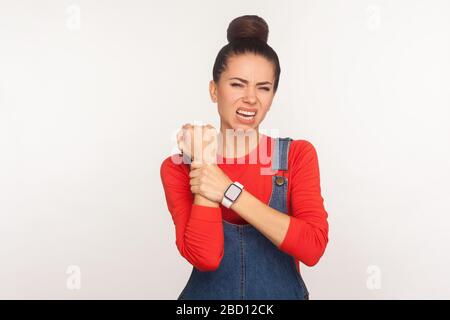 Polso incontrollato, rigidità muscolare. Ritratto di ragazza malsana con capelli bun in tute denim massaggiando mano dolorosa, soffrendo sindrome tunnel carpale. Foto Stock