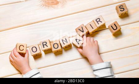 Bambino mette fuori la parola CORONAVIRUS. Coronavirus COVID-19 parola fatta da cubi di legno. SARS-COV-2, pandemia, sfondo epidemico. Bambini ed epidemia Foto Stock