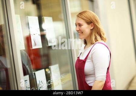 giovane donna che cerca in una finestra di agenti immobiliari Foto Stock