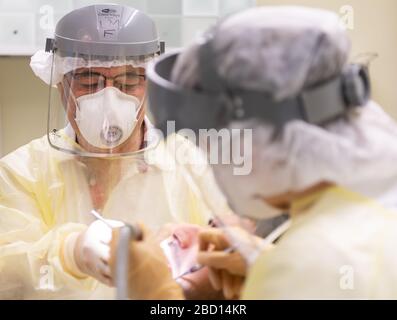Dresda, Germania. 3 aprile 2020. ILLUSTRAZIONE - il dentista Conrad Kühnöl (l) tratta un paziente corona nella sua pratica dentale con visiera, respiratore FFP3 e gown antivirale con i suoi assistenti dentali. (Posed scene) Credit: Robert Michael/dpa-Zentralbild/dpa/Alamy Live News Foto Stock