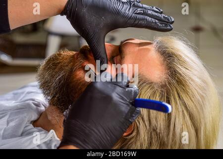 Grande tempo al barbiere. Barbuto al parrucchiere. Barbiere professionale con cliente maschile. Hipster con barba e baffi. Uomo vuole un nuovo acconciatura. Bellezza e moda. Uomo maturo al barbiere. Foto Stock