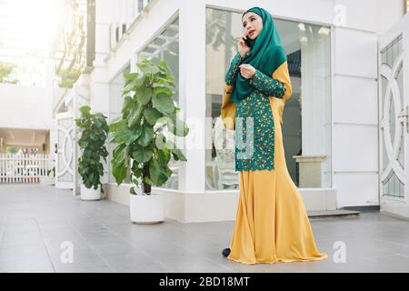 Bella giovane musulmana che cammina all'aperto e parla al telefono con un amico Foto Stock