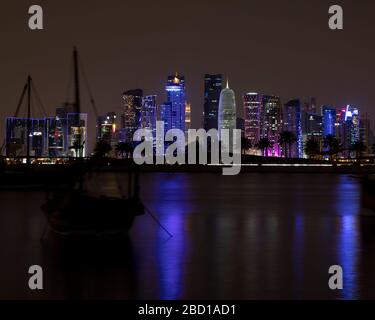 Una vista dello skyline di West Bay a Doha di notte con una barca tradizionale in primo piano. Foto Stock
