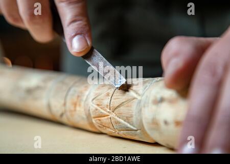 Processo di uomo che fa bastone di legno che cammina all'interno durante la quarantena. Bastone di legno intagliato sulla tavola usando il coltello Foto Stock