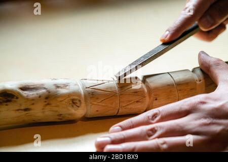 Processo di uomo che fa bastone di legno che cammina all'interno durante la quarantena. Bastone di legno intagliato sulla tavola usando il coltello Foto Stock