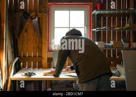 Processo di uomo che fa bastone di legno che cammina all'interno durante la quarantena. Bastone di legno intagliato sulla tavola usando il coltello Foto Stock