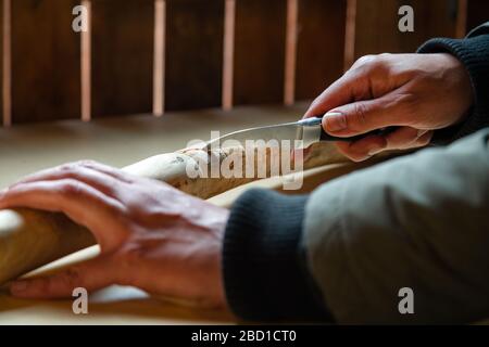 Processo di uomo che fa bastone di legno che cammina all'interno durante la quarantena. Bastone di legno intagliato sulla tavola usando il coltello Foto Stock