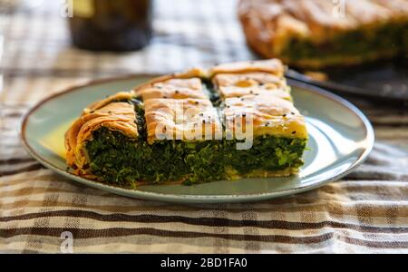 Concetto di cibo sano. Torta di spinaci o greco spanakopita che serve su sfondo tavolo da cucina, vista primo piano. Foto Stock