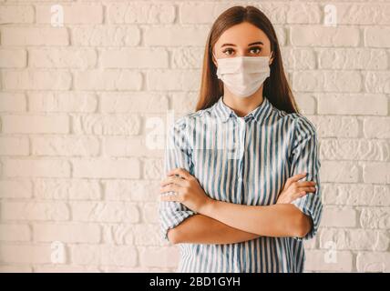 Giovane ragazza medico femminile in maschera protettiva sul viso tenendo le braccia incrociate in ospedale. Donna sicura malata in medicina maschera viso a casa quarantena. PE Foto Stock