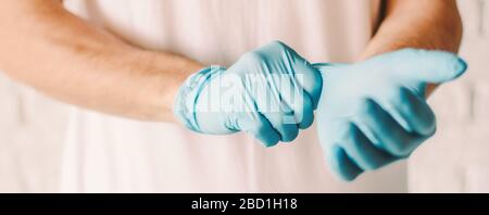 Uomo di vestizione banner che indossa guanti medici in lattice blu sulle mani. Medico professionista che indossa guanti protettivi sterili. Preparazione per esame paziente Foto Stock