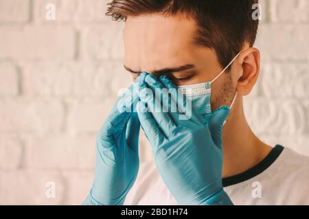 Frustrato uomo stanco in guanti protettivi sulle mani e maschera medica viso sensazione di mal di testa. Medico chirurgo esausto in maschera protettiva sul viso AN Foto Stock