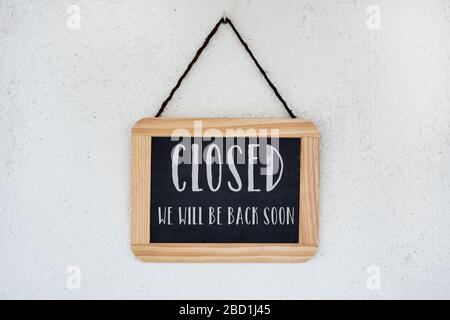 una lavagna con cornici in legno, con il testo chiuso, ci torneremo presto scritto, appeso da un muro bianco Foto Stock