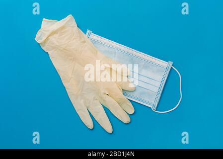 vista ad angolo elevato di un paio di guanti chirurgici monouso e di una maschera chirurgica monouso su sfondo blu Foto Stock