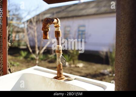 Vecchio rubinetto dell'acqua arrugginito su un lavandino in un cortile rurale Foto Stock