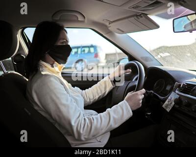 donna con maschera protettiva sul viso che guida auto durante una pandemia di coronavir Foto Stock