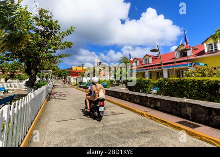 Coppia su ciclomotore, colorato Bourg des Saintes città, Terre de Haut, Iles Des Saintes, Les Saintes, Guadalupa, Isole Leeward, Caraibi Foto Stock