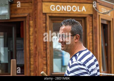 Primo piano di un gondoliere che indossa occhiali in una camicia strizzosa gondolieri alla stazione di S. Moise Gondola, Venezia, Italia Foto Stock