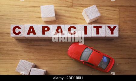Parola di capacità fatta di cubetti di legno su uno sfondo di legno con auto giocattolo rossa. Concetto di gestione logistica della capacità aziendale Foto Stock
