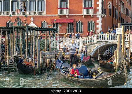 Due persone guardano da un balcone all'Hotel Danieli mentre i gondolieri prendono i turisti per un giro in gondola sul Canal Grande, Venezia Italia Foto Stock