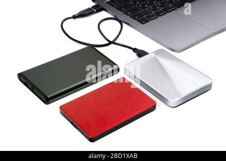Tre unità disco rigido portatili vicino a un notebook isolate in bianco. Una delle unità è collegata al computer portatile per il trasferimento dei dati. Foto Stock