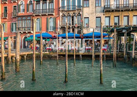 Per i pasti, si mangia all'aperto in un ristorante italiano di fronte ai pali in legno vicino a Rialto sul Canal Grande, Venezia, Italia Foto Stock