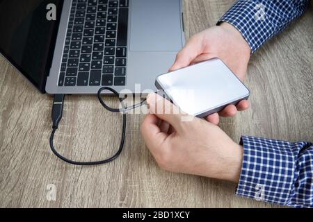 Le mani maschili in camicia blu a controllo scollegano un disco rigido esterno dal computer portatile. Foto Stock