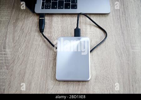 Disco rigido portatile collegato a un computer portatile su un tavolo di legno. Trasferimento o backup dei dati tra un computer portatile e un disco rigido. Foto Stock
