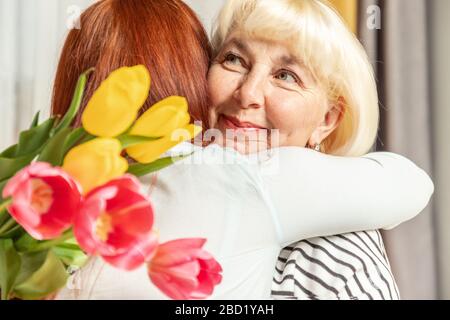 Madre e figlia giovane sono abbracciare. Figlia si congratula con la madre e dà un bouquet di fiori tulipani. Felice giorno della madre. Famiglia felice amorevole Foto Stock