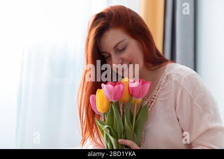 Bella giovane ragazza a capelli lunghi che tiene un bouquet di fiori freschi tulipani nelle sue mani e sniffing in camera. San Valentino, il concetto di compleanno Foto Stock