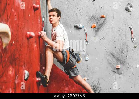 Scalatore sportivo che sale su roccia ripida, che sale su parete artificiale in interni. Sport estremi e concetto di bouldering Foto Stock