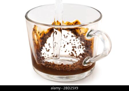 Versare acqua calda su caffè istantaneo in una tazza di erba isolata su bianco. Caffè parzialmente disciolto. Foto Stock