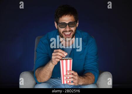 Ritratto di uomo bearded che indossa occhiali 3D mangiare popcorn mentre guarda il film a casa al buio, copy space Foto Stock