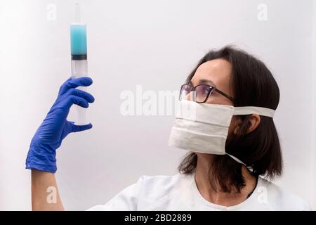 Un infermiere che indossa una maschera e guanti che tengono una siringa di vaccino anti virus in una clinica moderna Foto Stock